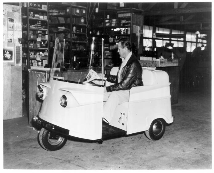 black and white photo of a man sitting on a white utility vehicle reading the newspaper in a warehouse