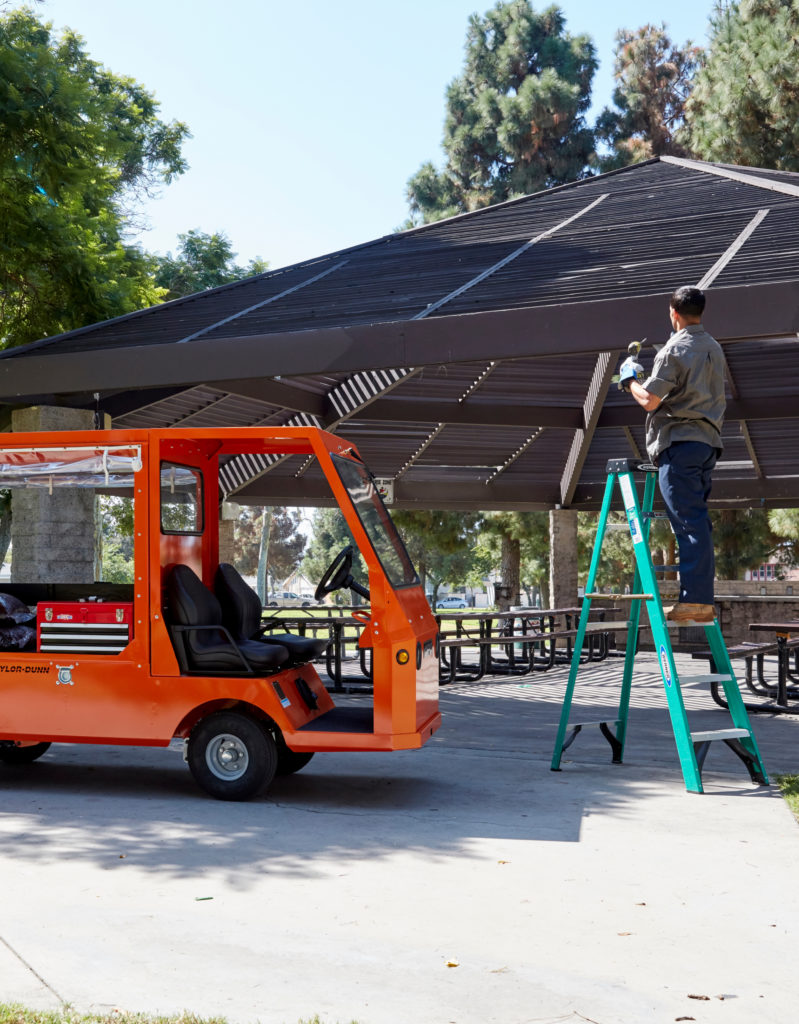 Man on a ladder next to an orange utility vehicle in the park