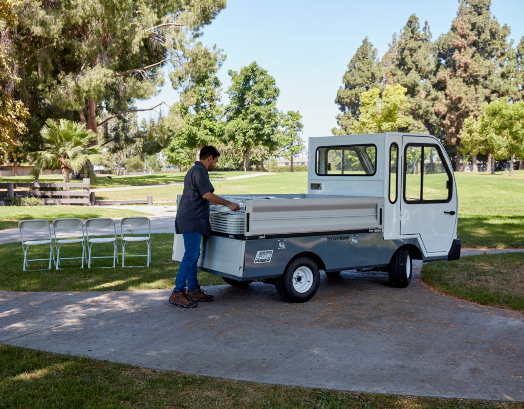 Man opening the tailgate of white utility vehicle in a park