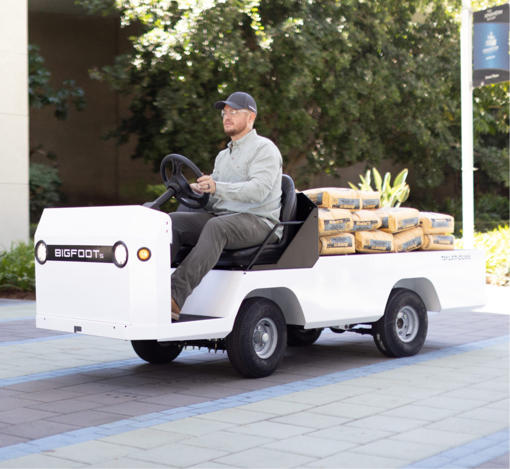 Man driving a white utility vehicle loaded with concrete mix