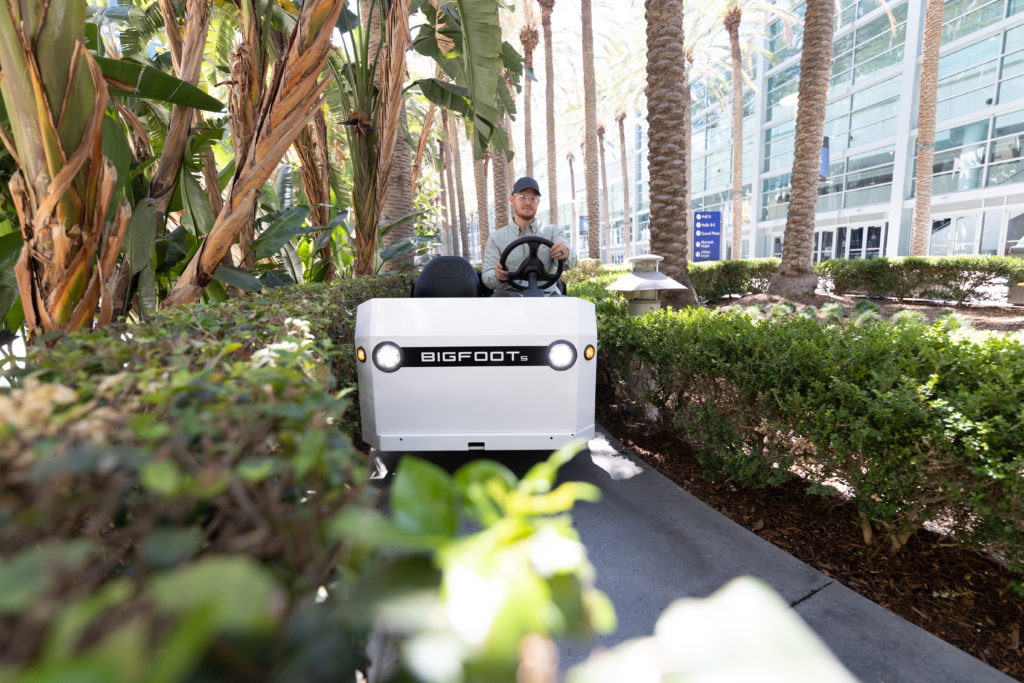 Man riding a white bigfoot utility vehicle through foliage