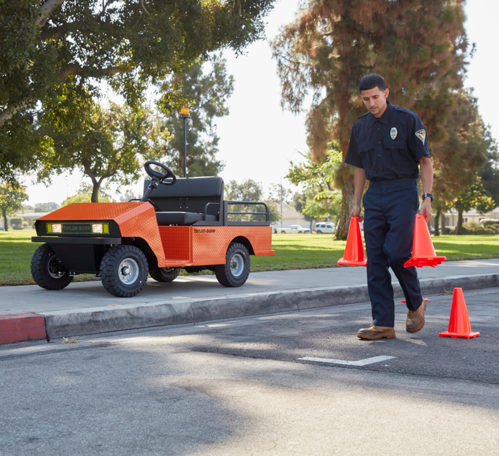 Man in uniform placing orange cones in the road next to an orange safety utility vehicle