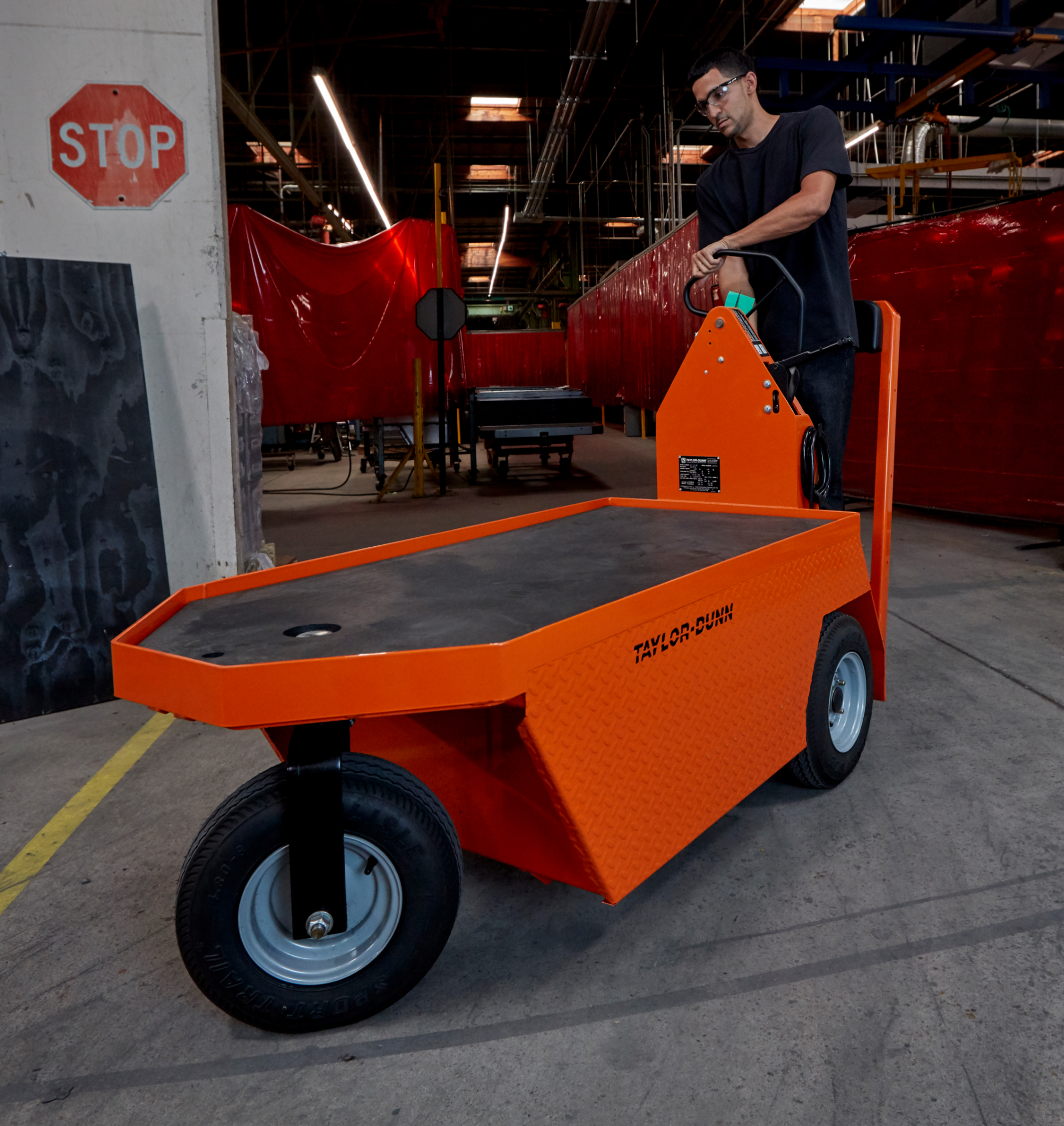 Man driving orange stock loading utility vehicle in a warehouse