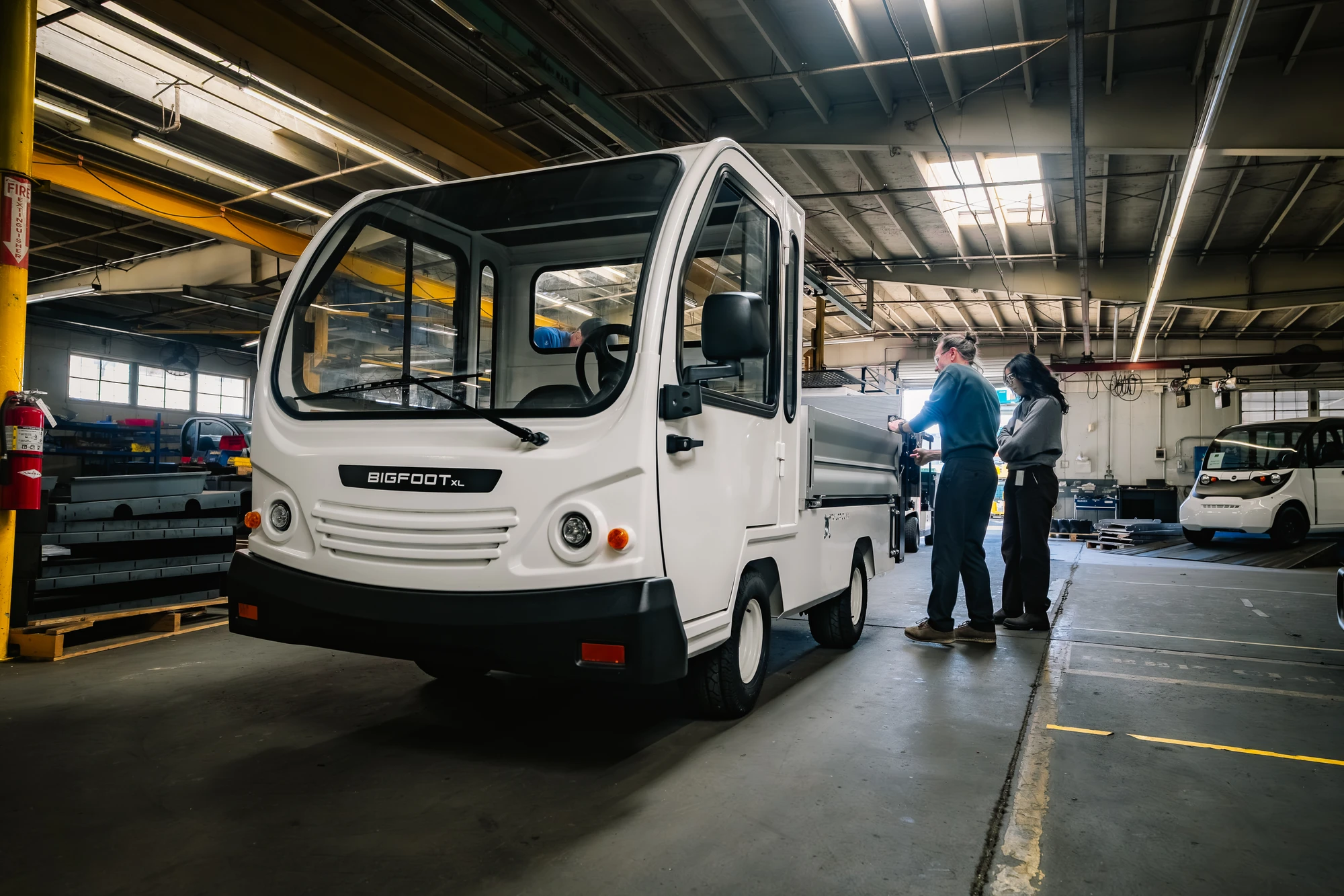 Taylor-Dunn-Bigfoot-XL-Liftgate-Tommy-Gate-Manufacturing-Indoors-Front-3Q-Cab-Workers-arm-opt
